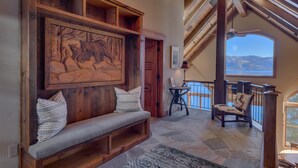 A spacious living area with a wooden bench, a large wall-mounted painting, and a view of a lake through a balcony. - Gonowabie Lodge - Crystal Bay Lakefront - TLUXP (Crystal Bay)