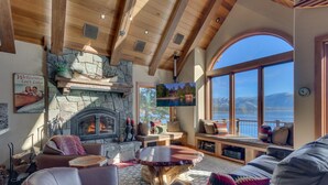 A cozy living room with a stone fireplace, comfortable seating, and a large window overlooking a lake. - Gonowabie Lodge - Crystal Bay Lakefront - TLUXP (Crystal Bay)
