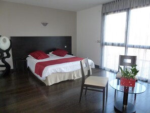 Relax in comfort with a large bed, a glass table, and a chair, set against a backdrop of a large window.