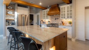 A spacious kitchen with a large island, wooden beams, and white cabinetry.