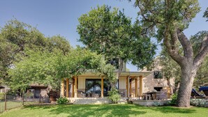 A house with a covered patio, a brick exterior, and a large tree in the front yard.