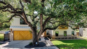 A two-story house with a large tree in front, a garage, and a well-maintained lawn.