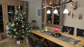 A dining area with a wooden table, chairs, a Christmas tree, and a window with curtains.