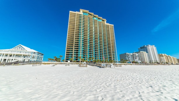 A beachfront hotel with a high-rise structure, a beach in the foreground, and other buildings in the background. - Parking level!  Lazy river/Slide. New to the rental market!! (Orange Beach)