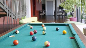 Een biljart met ballen in een kamer met een trap, een eethoek en potplanten.