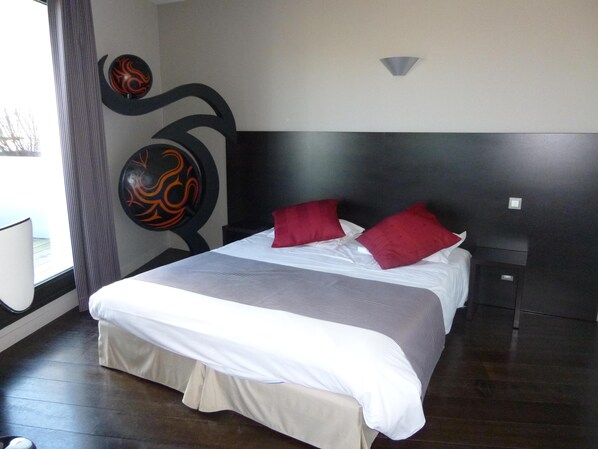 A hotel room with a bed, a headboard, a wall decoration, and a window.