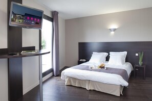 A modern hotel room with a large bed, a bedside table, a TV mounted on a wall, and a window with curtains.
