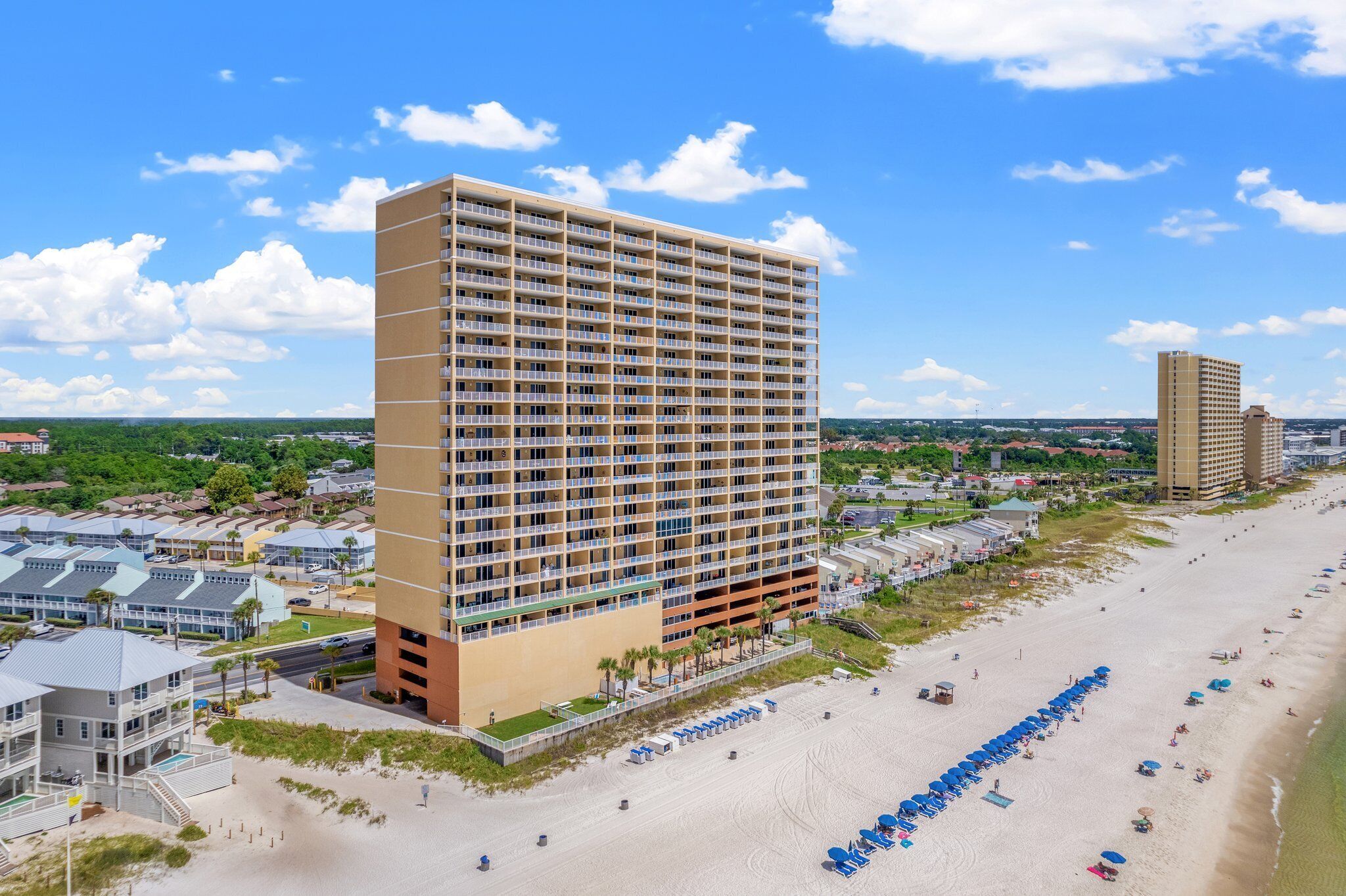 A high-rise hotel with multiple floors, a beachside location, and a row of blue umbrellas on the beach.