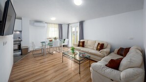Een moderne woonkamer met een bank, een glazen salontafel en een eethoek met een tafel en stoelen.