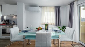 Een moderne eetruimte met een glazen tafel, witte fauteuils en een keuken op de achtergrond.