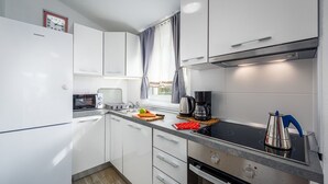 Een compacte keuken met witte kastjes, een magnetron, koffiezetapparaat en waterkoker op het aanrecht.