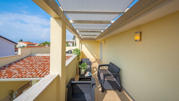 Een balkon met een betegeld dak, zitplaatsen buiten en een plant in pot.