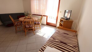 A room with a bed, a dining table with chairs, a TV, and a window with curtains.