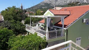 A green building with a red-tiled roof, a balcony with white railings, and a view of a mountain in the background. - Apartments Clementina Sunrise (Orebic)