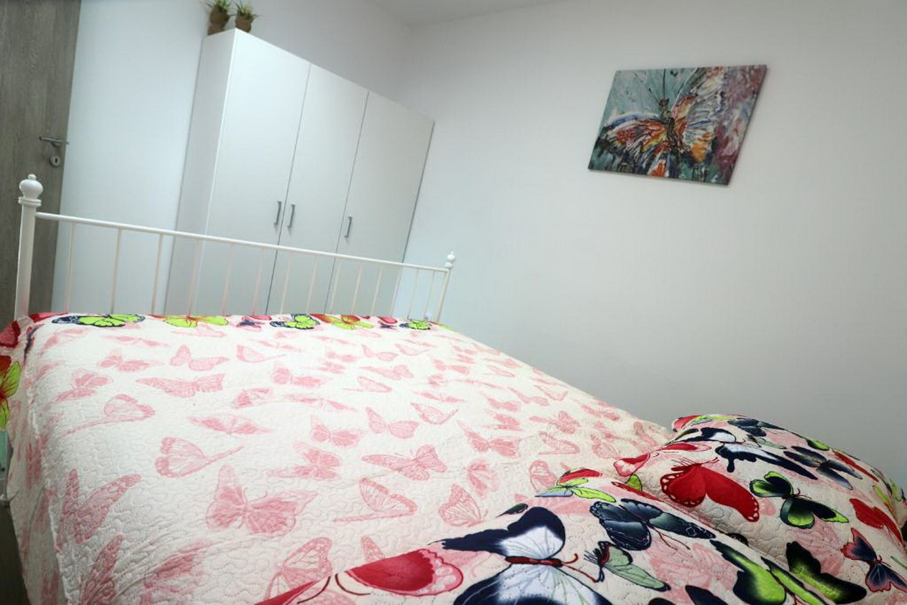 A bedroom with a bed, a white wardrobe, and a painting on the wall.