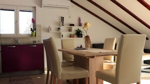 A dining area with a wooden table and four chairs, a kitchen with purple cabinets, and a window with a potted plant. - Apartments Clementina Sunrise (Orebic)