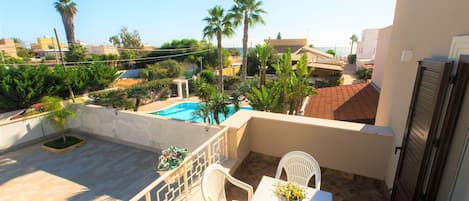 A balcony with a table and chairs, overlooking a swimming pool and palm trees.
