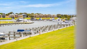 A marina with boats docked, a grassy area, and a row of buildings in the background. - Hindmarsh Island - Waterfront Luxury, Wi-Fi, Linen (Hindmarsh Island)