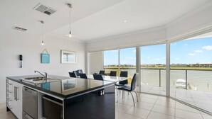 A modern kitchen with a large island, a dining area with chairs, and a view of a body of water. - Hindmarsh Island - Waterfront Luxury, Wi-Fi, Linen (Hindmarsh Island)