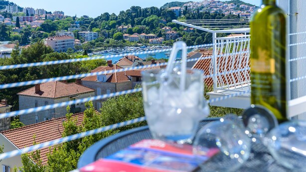 Ein Balkon mit Essplatz, mit Blick auf eine Küstenstadt und ihre Gebäude und Boote.