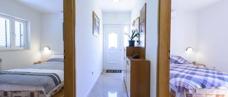 A hallway with two bedrooms, each with a bed and bedside table. A wooden cabinet is placed between the rooms.