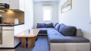 Ein kompakter Wohnraum mit einer Küchenzeile, einem Sofa, einem kleinen Tisch und einem Fenster, das für natürliches Licht sorgt.