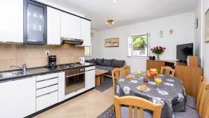 Eine kleine Küche mit Herd, Spüle und Mikrowelle. Im Wohnbereich befindet sich ein Esstisch mit Stühlen sowie eine Couch.