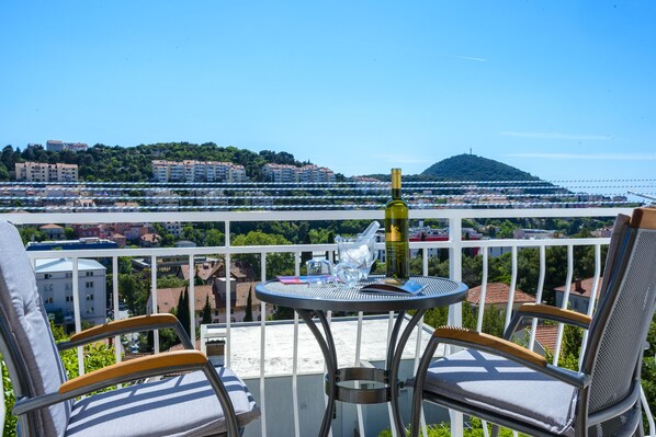 A balcony with a table and chairs, overlooking a coastal cityscape with buildings and a hill.