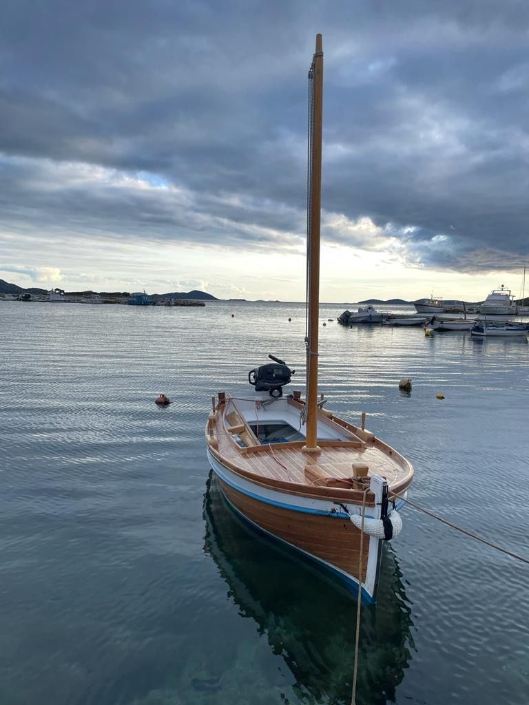 A wooden boat docked at a calm harbor with other boats in the background.