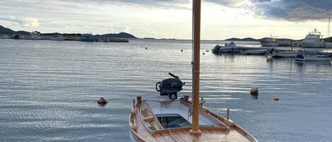 A wooden boat docked at a calm harbor with other boats in the background.