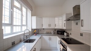 Eine moderne Küche mit weißen Schränken, einer Edelstahl-Spüle, einer schwarzen Induktionskochplatte und einem Fenster für natürliches Licht.