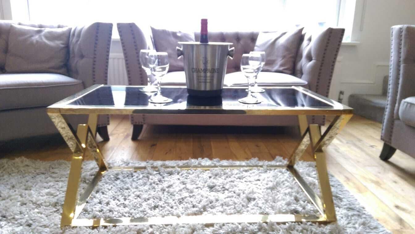 A glass-top table with a champagne bucket and glasses, a fluffy white rug, and a sofa in the background.