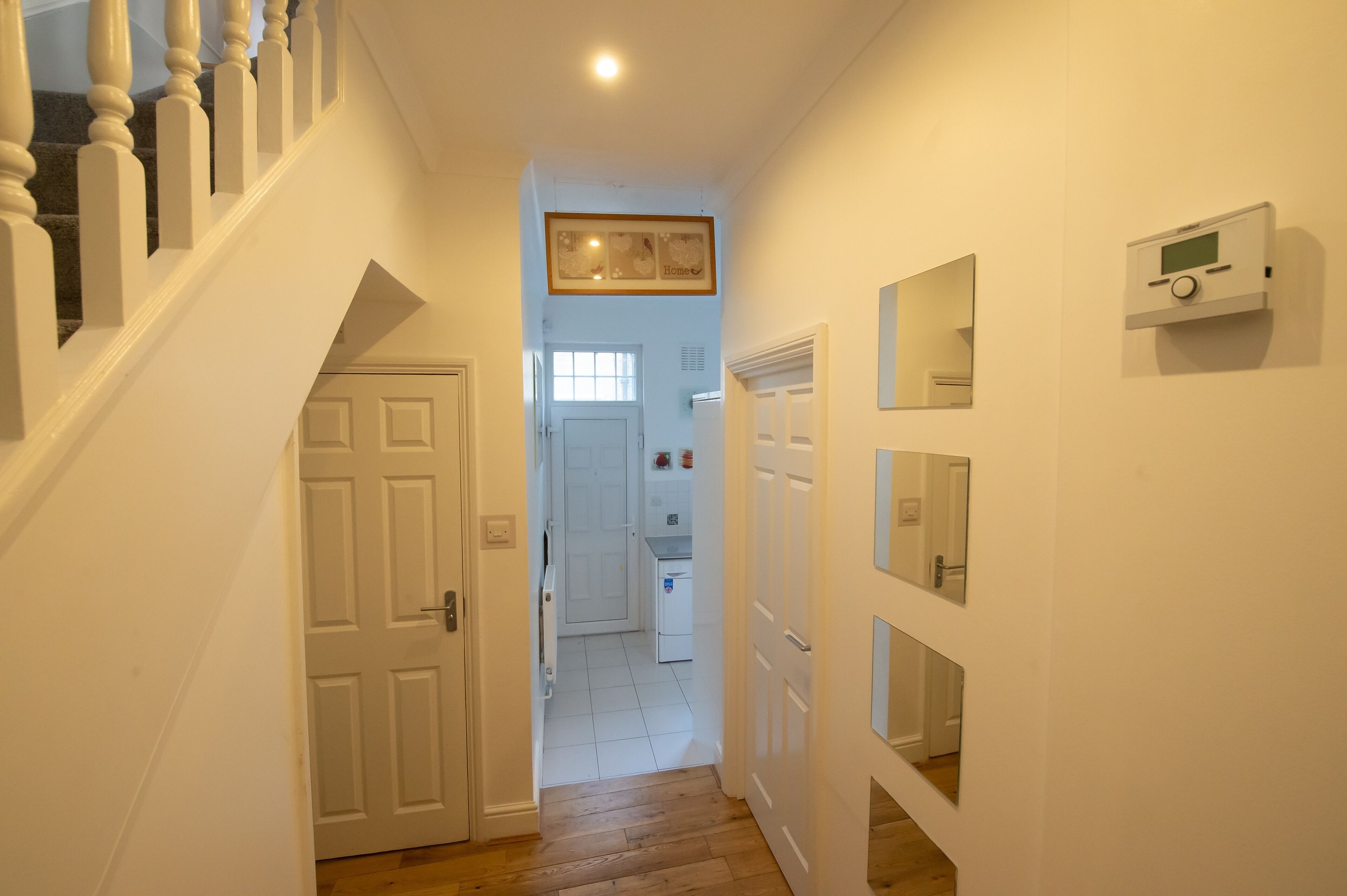 Un pasillo con una escalera, una puerta que da a una cocina y un termostato en la pared.