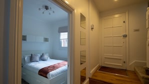 Ein Schlafzimmer mit Bett, Deckenventilator, Fenster und einer zur Treppe führenden Tür.