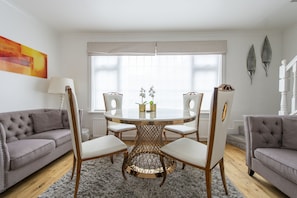 Un coin repas avec une table ronde, quatre chaises, un canapé gris et une fenêtre avec des rideaux.