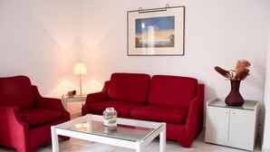 A living room with a red sofa set, a glass coffee table, a lamp, a framed picture on the wall, and a cabinet with a vase.