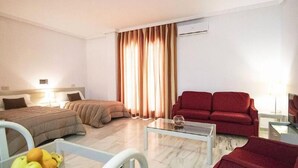Habitación de hotel con dos camas, un sofá rojo, una mesa de centro de vidrio y un frutero.