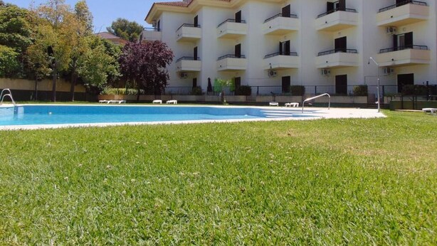 Un hotel con piscina, varios balcones y un césped bien cuidado.
