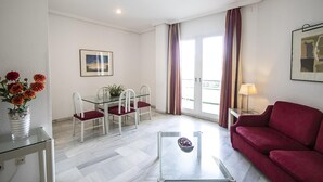 A modern living room with a glass coffee table, a red sofa, a dining area with a glass table and chairs, and a balcony with curtains. - Junior Suite Solarium (Mairena del Aljarafe)