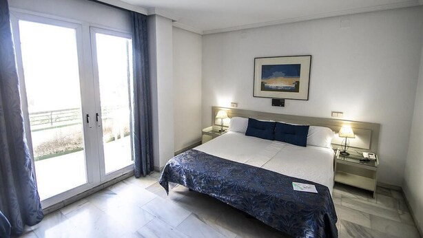 A hotel room with a large bed, two bedside tables with lamps, a painting on the wall, and a sliding glass door to the outside. - Winter Suite       . (Mairena del Aljarafe)