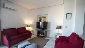 A living room with a red sofa, a television, a fireplace, and a small table with a lamp. - Winter Suite       . (Mairena del Aljarafe)