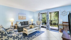 A living room with a sofa, coffee table, and a view of the outdoors. - Charming Beach Escape! Steps from the Beach (Hilton Head Island)