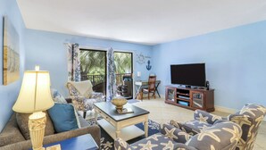 A living room with a sofa, armchair, TV, and a table with a lamp. - Charming Beach Escape! Steps from the Beach (Hilton Head Island)