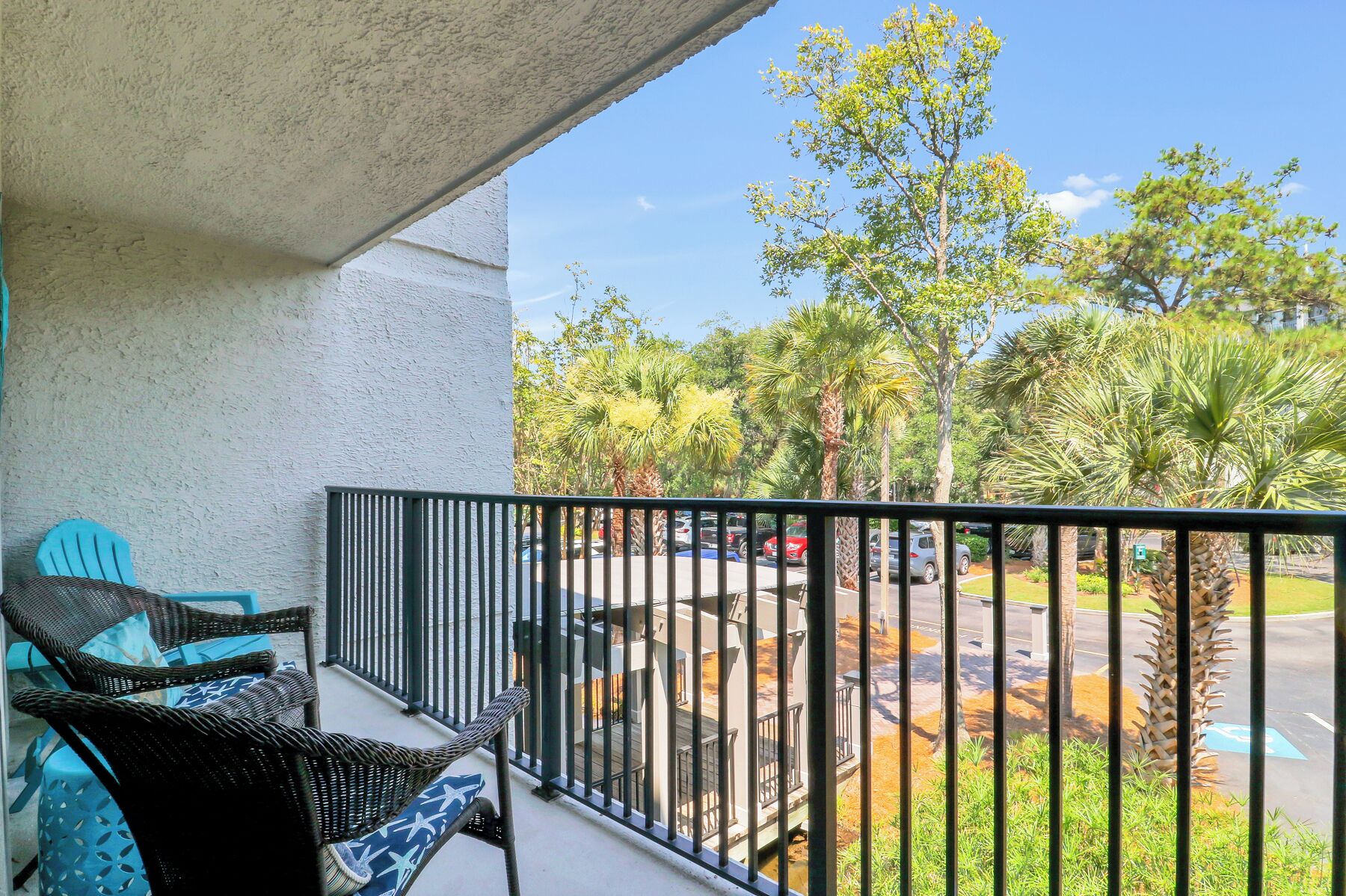 A balcony with wicker furniture and a view of a parking lot and trees.