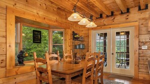L’intérieur d’un chalet en bois, avec une table à manger, des chaises, une figurine d’ours et une vue sur l’extérieur.