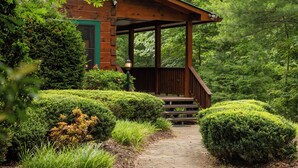 Une cabane en bois dotée d’un porche, entourée d’une végétation luxuriante et bordée d’un sentier en pierre.