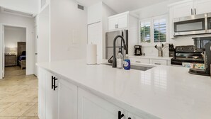 A modern kitchen with white cabinetry, stainless steel appliances, and a marble countertop.