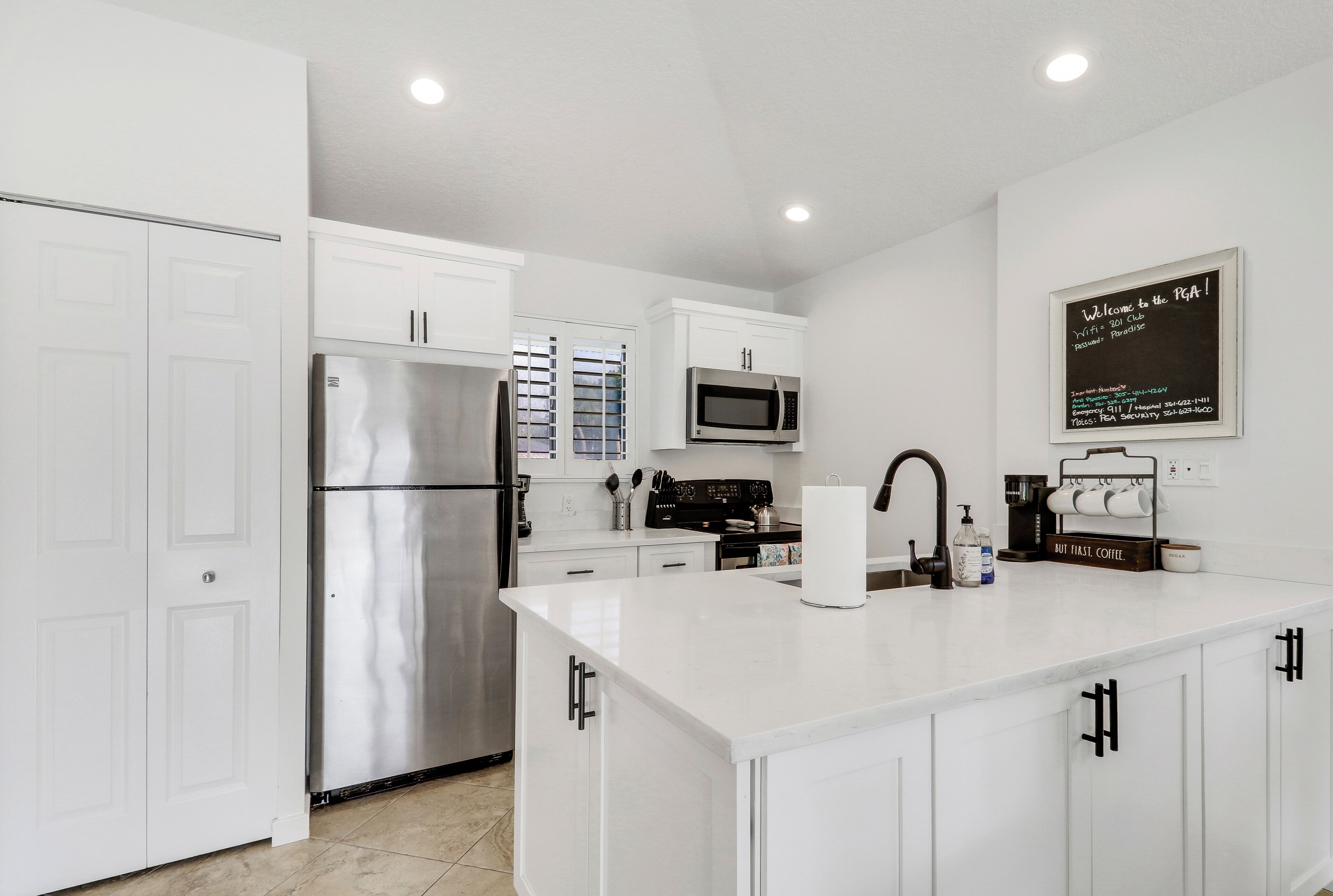 A modern kitchen with white cabinetry, stainless steel appliances, and a chalkboard sign.
