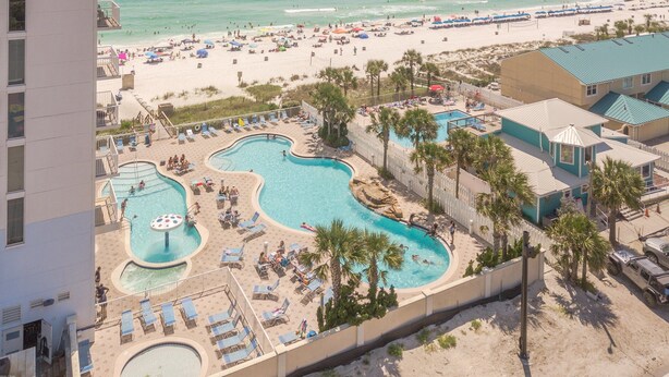 A resort with a pool area, beach, and a building with a blue roof.