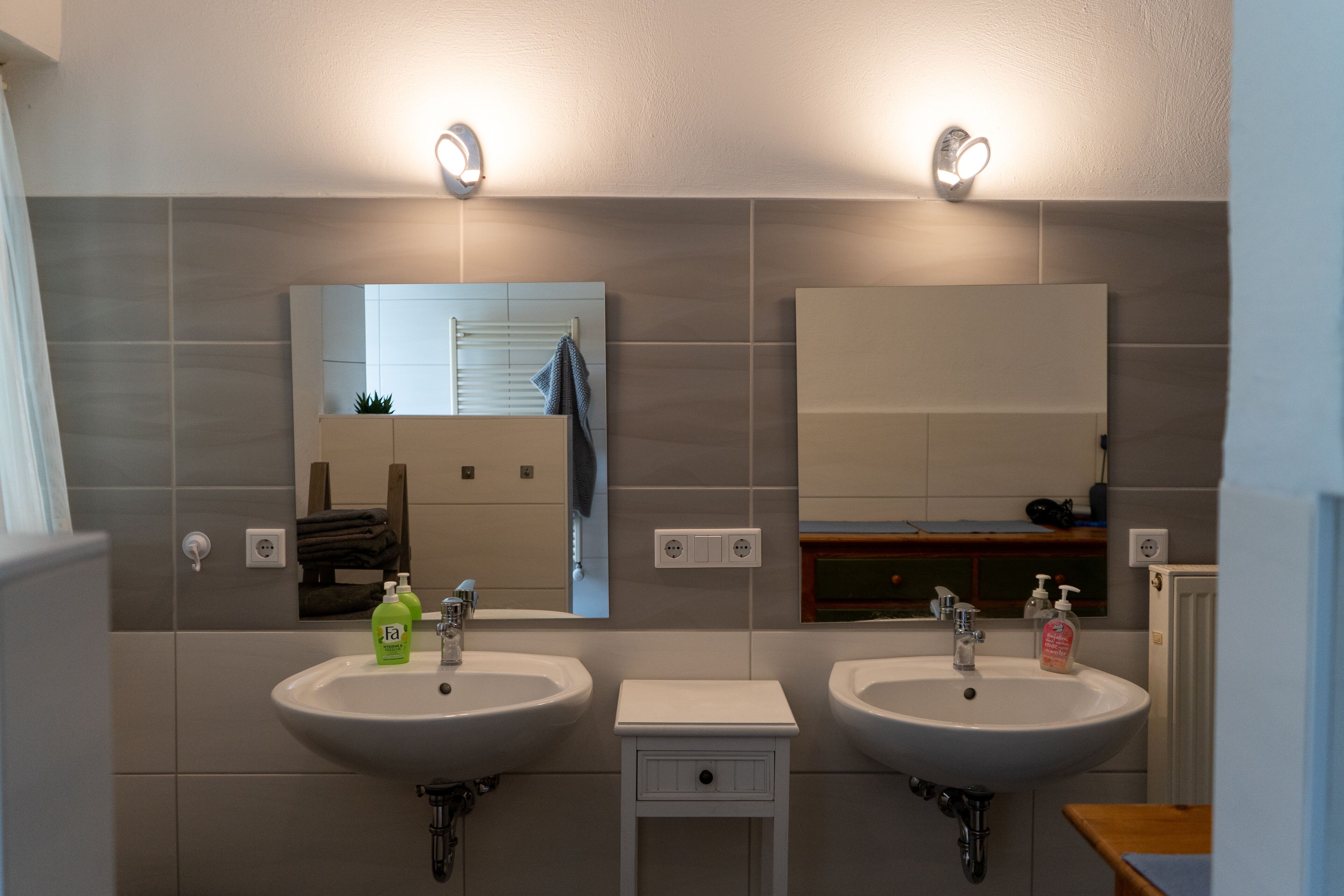 Casa de banho com duas pias, espelho e um pequeno armário.